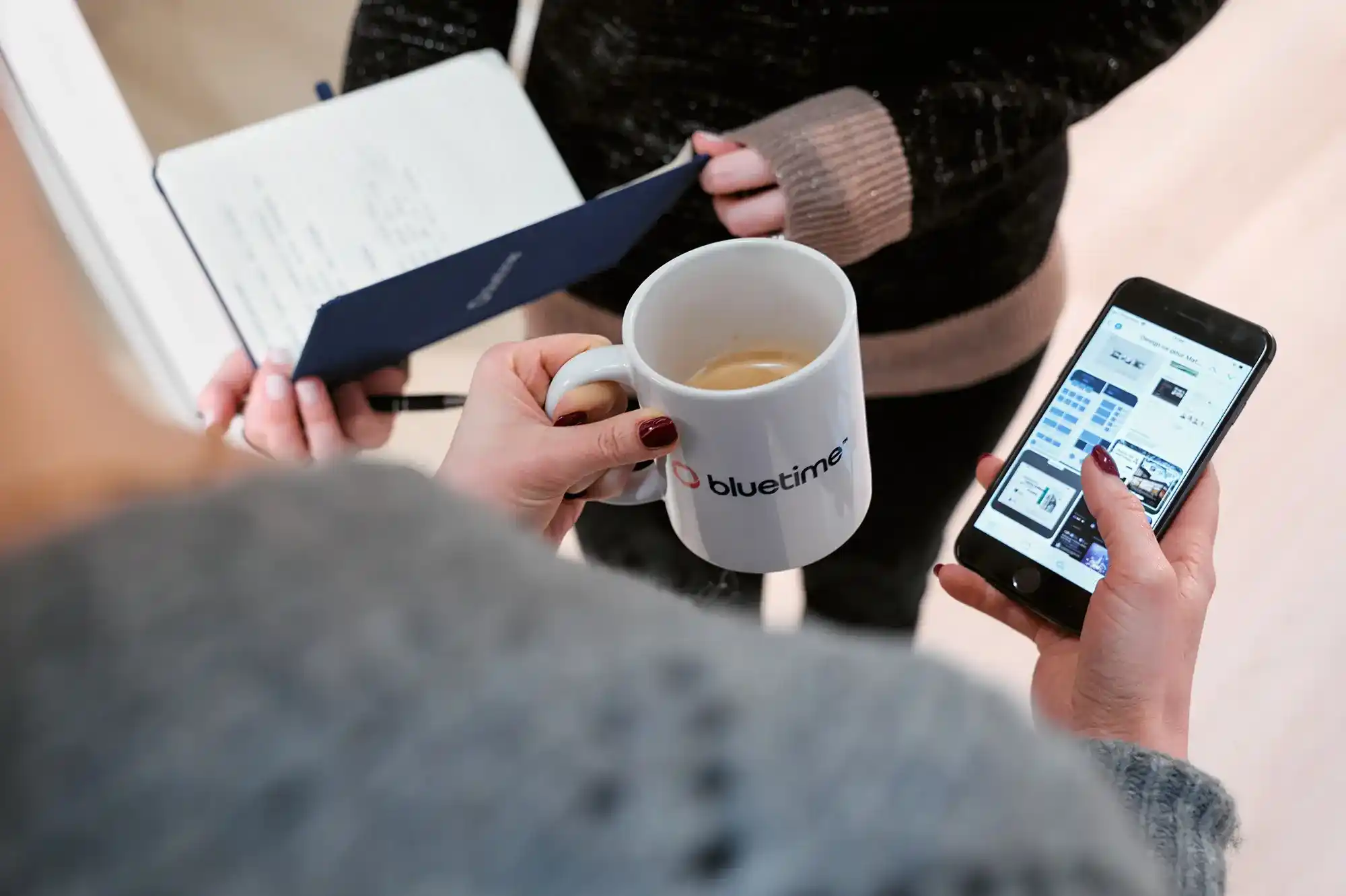 Personne tenant une tasse blanche au logo «&nbsp;Bluetime&nbsp;» et un smartphone affichant un site web